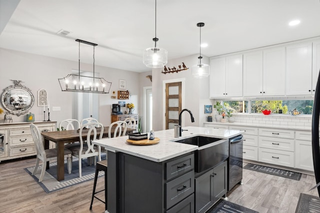 kitchen featuring white cabinets, a kitchen island with sink, a sink, visible vents, and gray cabinets