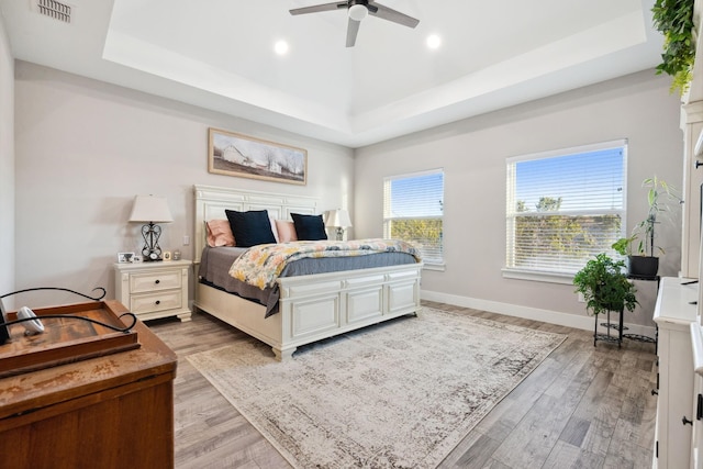 bedroom featuring light wood finished floors, baseboards, visible vents, and a raised ceiling