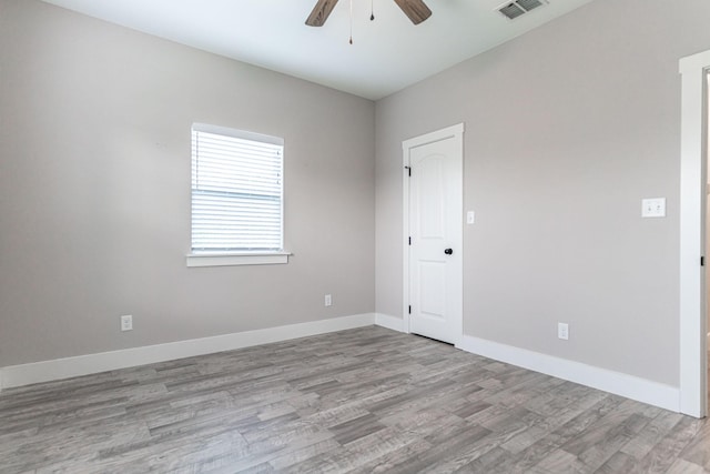 empty room with baseboards, a ceiling fan, wood finished floors, and visible vents
