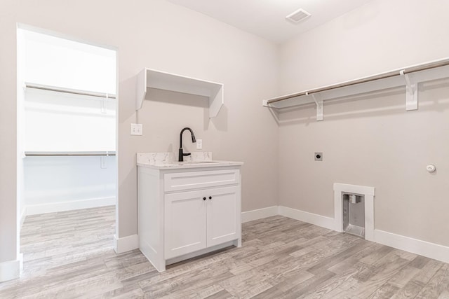 clothes washing area with electric dryer hookup, visible vents, a sink, and light wood finished floors
