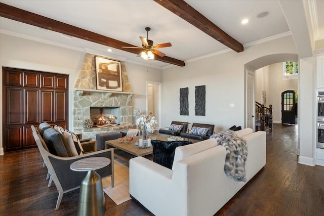 living room with arched walkways, beamed ceiling, a ceiling fan, dark wood-type flooring, and a stone fireplace