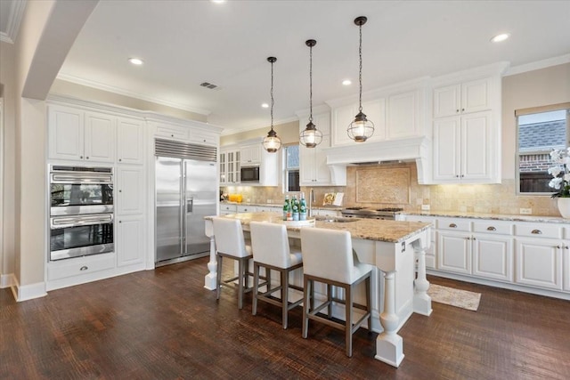 kitchen featuring built in appliances, white cabinetry, tasteful backsplash, a kitchen breakfast bar, and crown molding