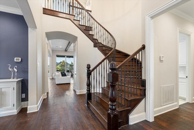 entryway with arched walkways, wood finished floors, crown molding, baseboards, and stairway