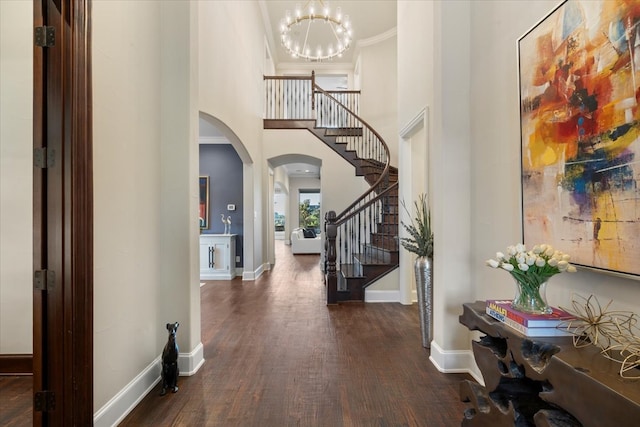 foyer with arched walkways, wood finished floors, a high ceiling, a chandelier, and stairs