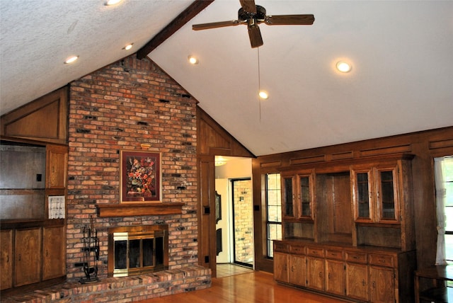 unfurnished living room with wood walls, wood finished floors, a brick fireplace, high vaulted ceiling, and ceiling fan