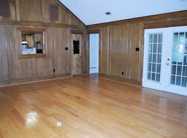 empty room featuring wood walls, lofted ceiling, french doors, and wood finished floors