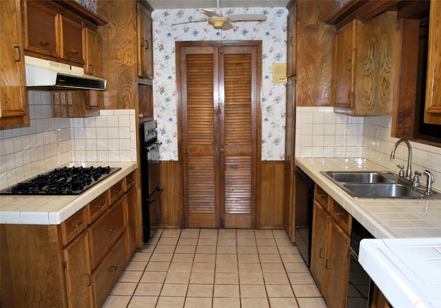 kitchen with wallpapered walls, wainscoting, under cabinet range hood, and a sink