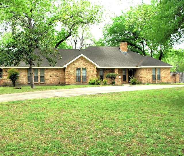 ranch-style home featuring brick siding, roof with shingles, a chimney, and a front yard