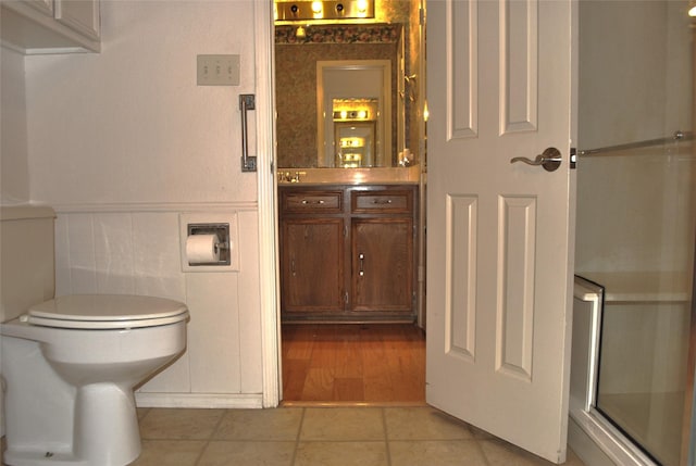 bathroom with wainscoting, toilet, a shower with door, and vanity