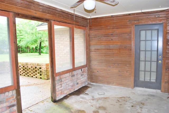interior space with wooden walls, a ceiling fan, and unfinished concrete flooring