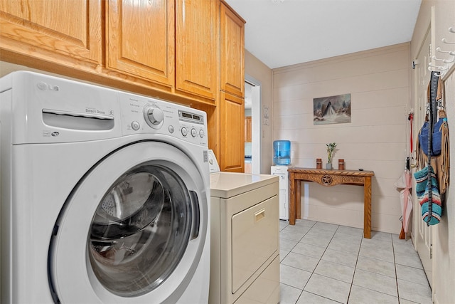 laundry room with wood walls, independent washer and dryer, light tile patterned floors, and cabinet space