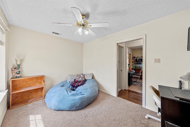 living area with visible vents, carpet floors, a textured ceiling, and ceiling fan