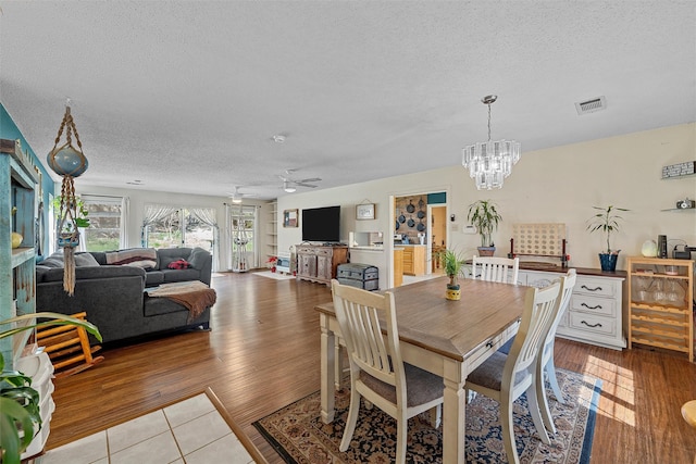 dining room featuring wood finished floors, a textured ceiling, visible vents, and ceiling fan with notable chandelier