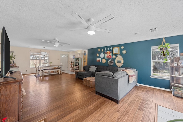 living area featuring wood finished floors, visible vents, a textured ceiling, and ceiling fan