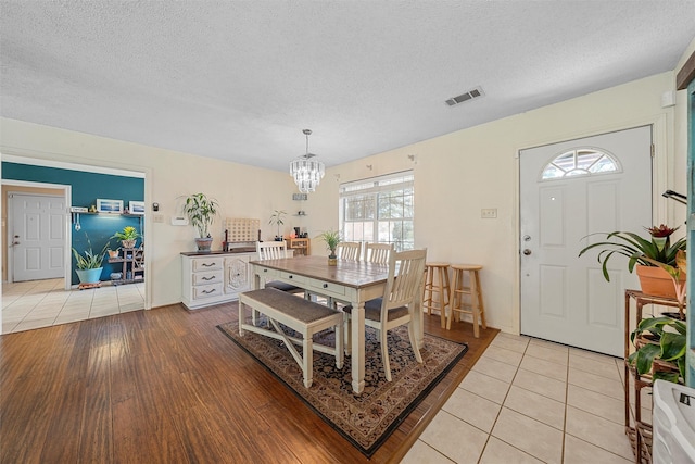 dining area featuring visible vents, a textured ceiling, a notable chandelier, and light tile patterned floors