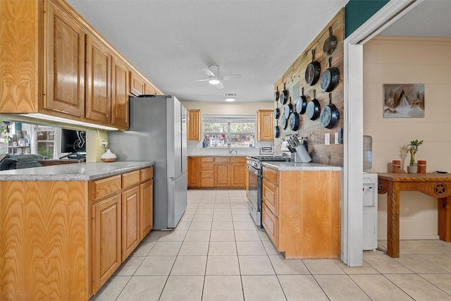 kitchen with a textured ceiling, appliances with stainless steel finishes, ceiling fan, and light tile patterned floors