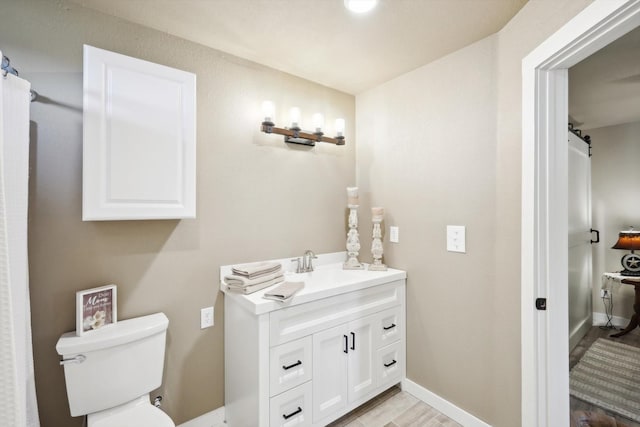 bathroom featuring baseboards, wood finished floors, toilet, and vanity