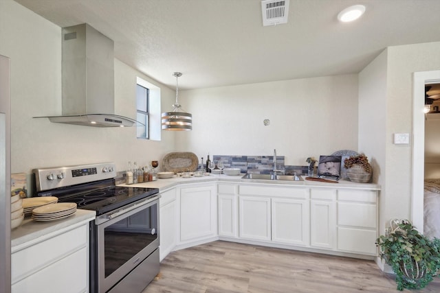 kitchen with a sink, stainless steel electric range oven, light wood-type flooring, white cabinetry, and wall chimney range hood