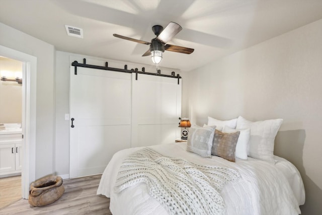bedroom with light wood finished floors, a closet, visible vents, and a barn door