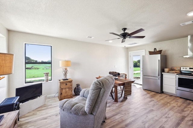 living room with ceiling fan, a textured ceiling, visible vents, and light wood-type flooring
