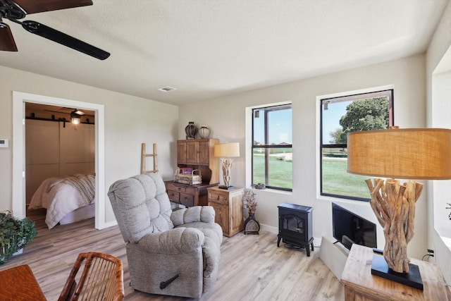 sitting room featuring a wood stove, ceiling fan, visible vents, baseboards, and light wood-type flooring