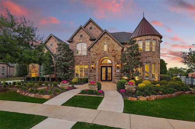 french country home with stone siding, french doors, fence, brick siding, and a standing seam roof