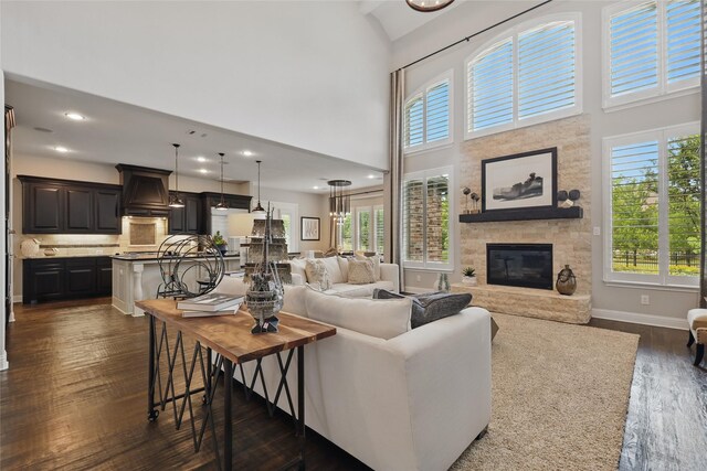 living area with baseboards, a towering ceiling, a fireplace, and dark wood-type flooring