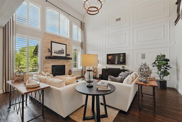 living area featuring a fireplace, a high ceiling, dark wood-style floors, and an inviting chandelier