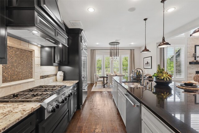 kitchen featuring light stone counters, tasteful backsplash, a sink, decorative light fixtures, and appliances with stainless steel finishes