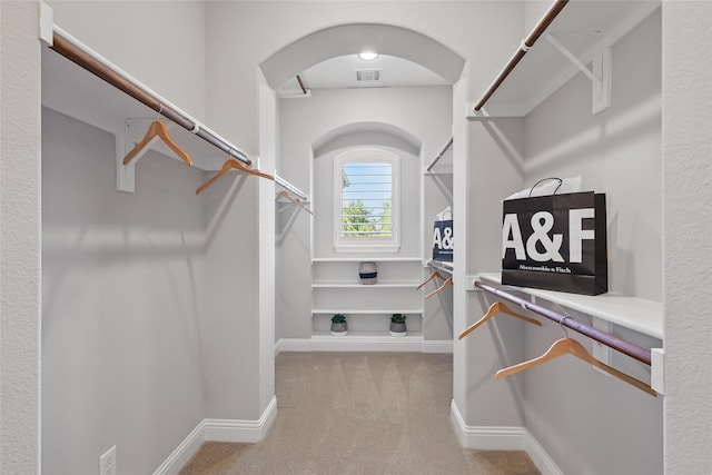 spacious closet with arched walkways, visible vents, and carpet