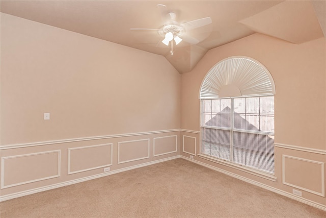 carpeted empty room featuring wainscoting, vaulted ceiling, ceiling fan, and a decorative wall