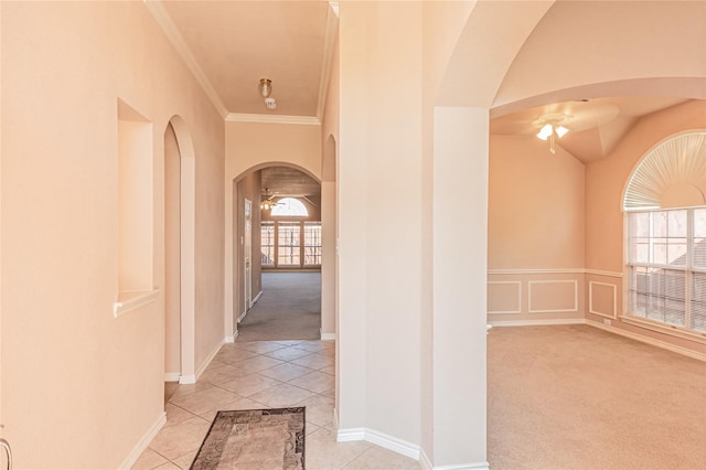 hall with light carpet, arched walkways, light tile patterned floors, and crown molding