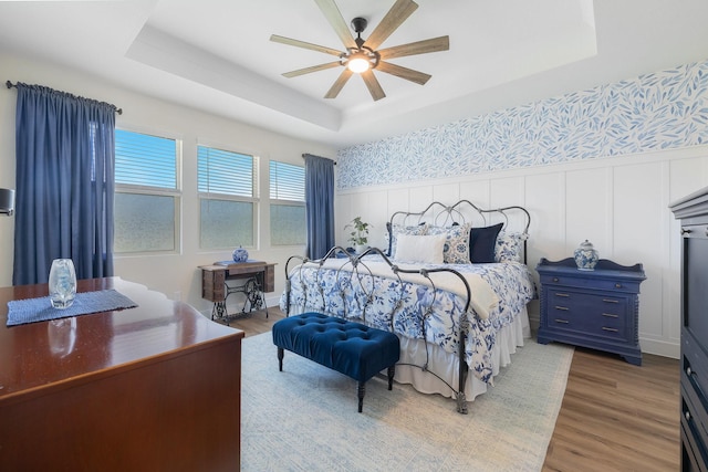 1236 Monterra Way, Fate, TX 75087 - bedroom featuring a raised ceiling, light wood-style flooring, a wainscoted wall, a decorative wall, and a ceiling fan