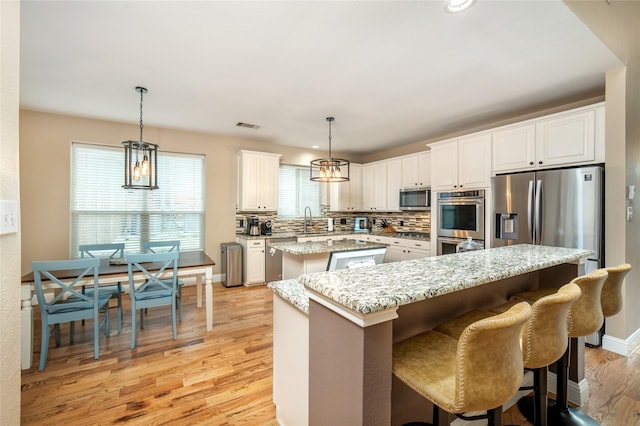 7612 Trevino Dr, Plano, TX 75025 - kitchen featuring appliances with stainless steel finishes, a center island, light wood-type flooring, a sink, and white cabinets