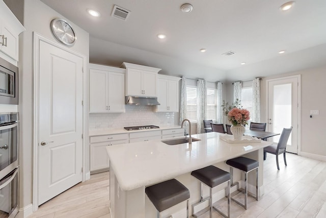 kitchen with visible vents, under cabinet range hood, a sink, and light wood-style floors