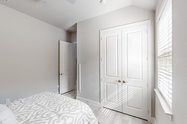 bedroom featuring lofted ceiling, light wood finished floors, a closet, baseboards, and ceiling fan