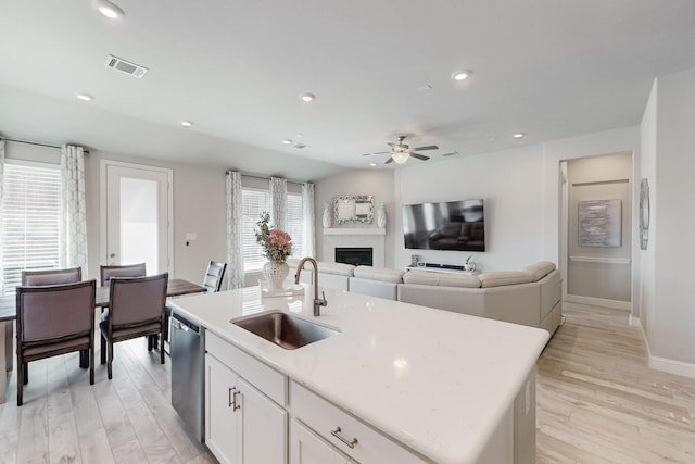 kitchen featuring a ceiling fan, a sink, dishwasher, light wood-style flooring, and a fireplace