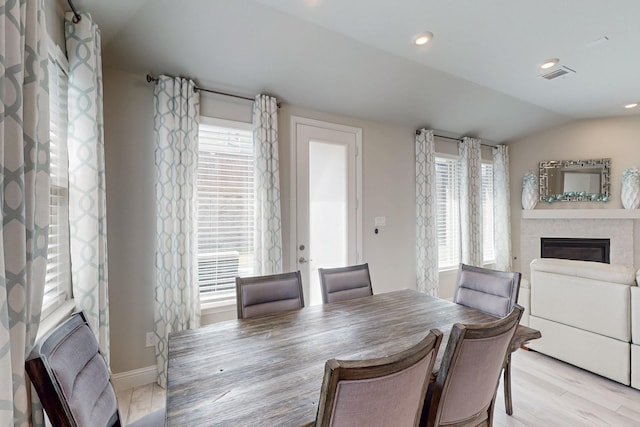 dining space with vaulted ceiling, light wood-style flooring, a glass covered fireplace, and a wealth of natural light