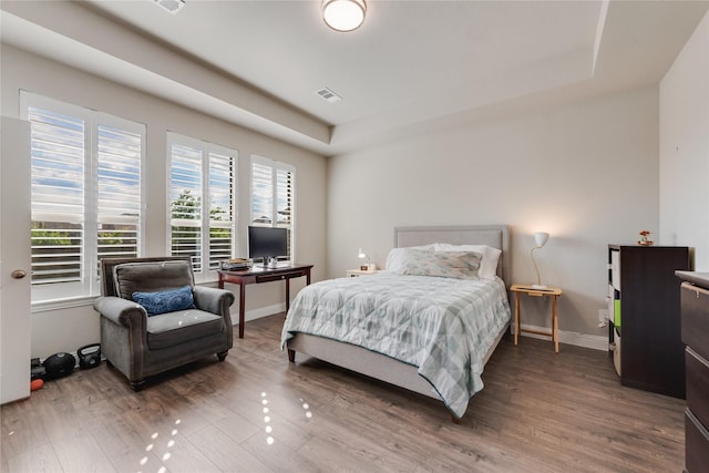 bedroom with baseboards, wood finished floors, visible vents, and a raised ceiling