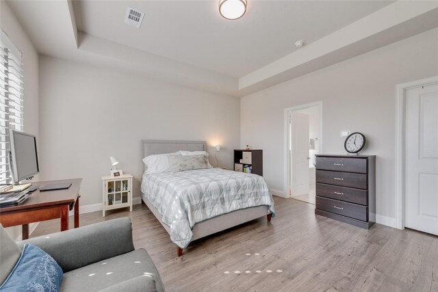 bedroom featuring a raised ceiling, wood finished floors, visible vents, and baseboards