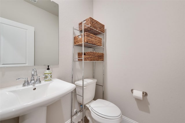 half bath featuring visible vents, toilet, baseboards, and a sink