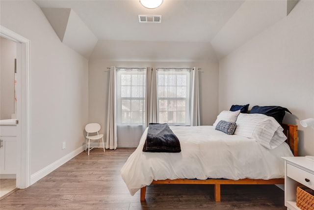 bedroom with light wood-style flooring, baseboards, visible vents, lofted ceiling, and ensuite bath