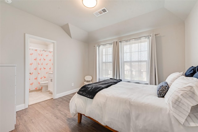 bedroom with vaulted ceiling, wood finished floors, baseboards, ensuite bath, and visible vents