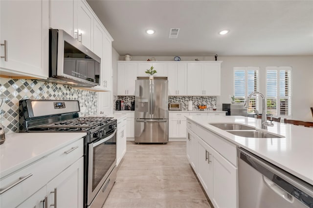 kitchen with white cabinets, stainless steel appliances, light countertops, a sink, and tasteful backsplash