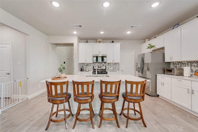 kitchen featuring stainless steel appliances, a sink, visible vents, decorative backsplash, and light countertops