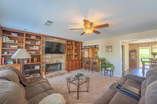 carpeted living room featuring a stone fireplace, visible vents, a ceiling fan, and baseboards