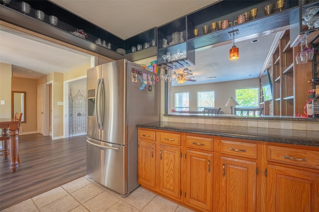 kitchen featuring brown cabinetry, dark stone counters, light tile patterned floors, and stainless steel fridge with ice dispenser