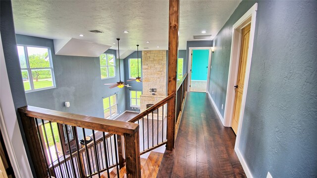 corridor with a textured wall, dark wood finished floors, baseboards, and visible vents