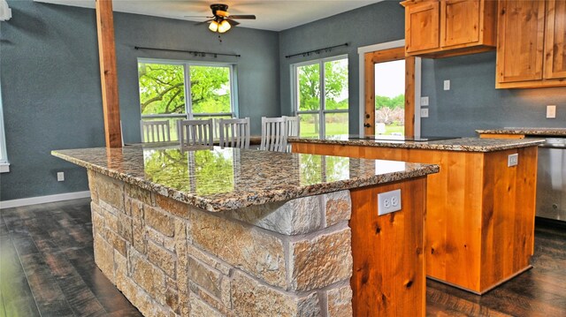 kitchen featuring stone countertops, ceiling fan, dark wood-style floors, a center island, and brown cabinets