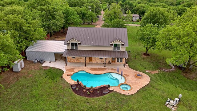 back of house featuring an in ground hot tub, a standing seam roof, an outdoor pool, a patio, and stone siding